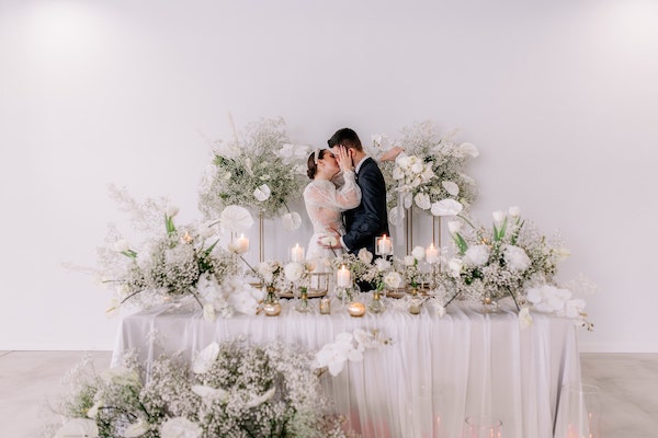 A groom and a bride kissing next to the table decorated with flowers