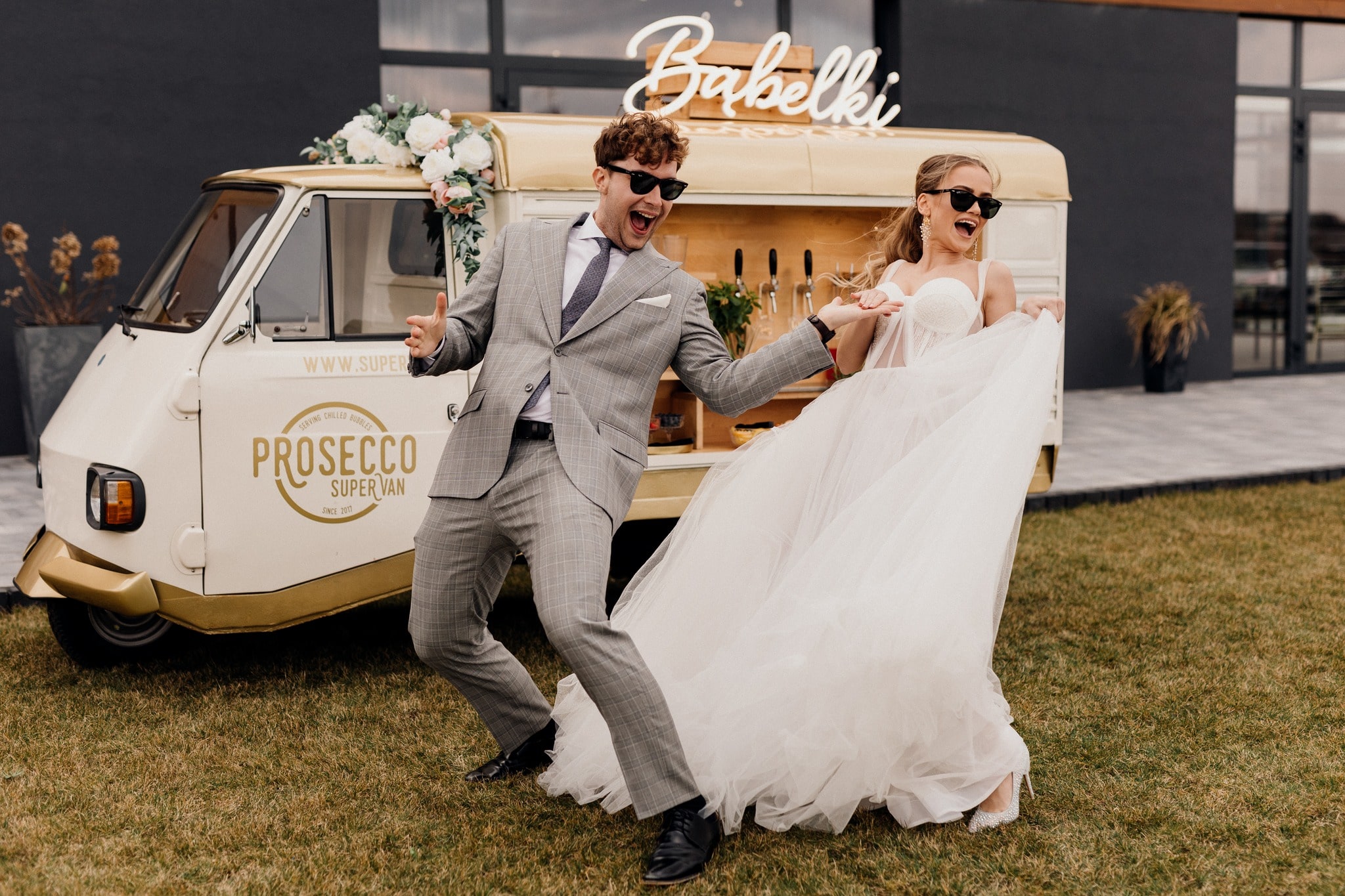 A wedding couole dancing in the garden in front of prosecco van