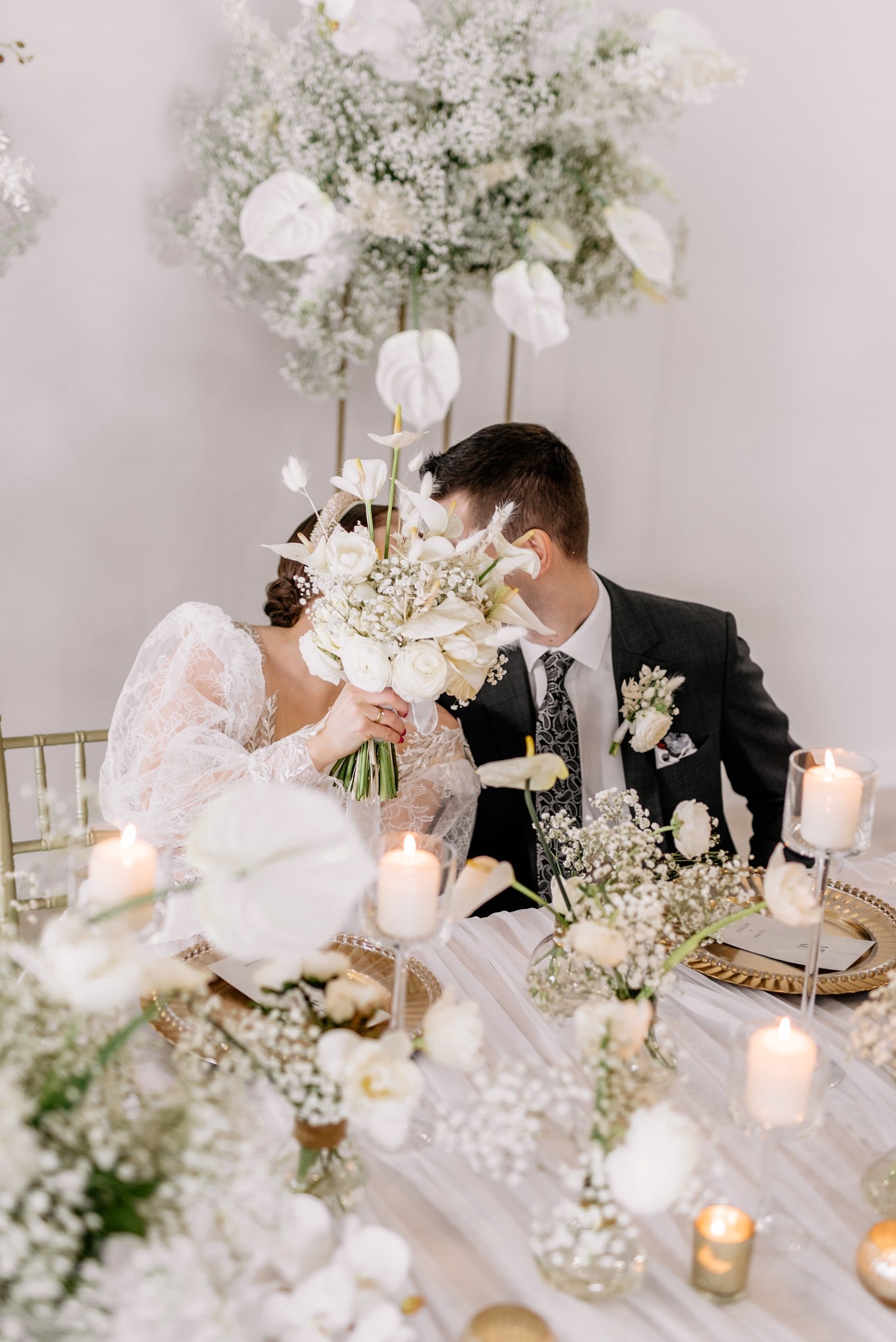 A bride and a groom sitting at a decorated table and kissing
